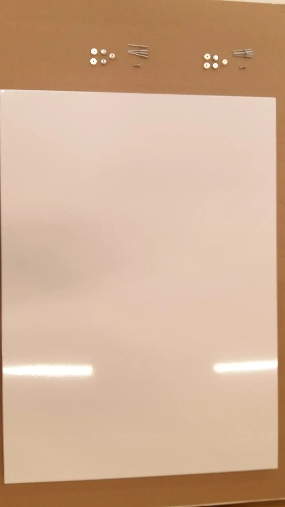 Weiße Seitenwand von Remeha auf braunem Hintergrund. Darunter liegen verschiedene Metallteile, möglicherweise zur Befestigung oder Montage der Wand.